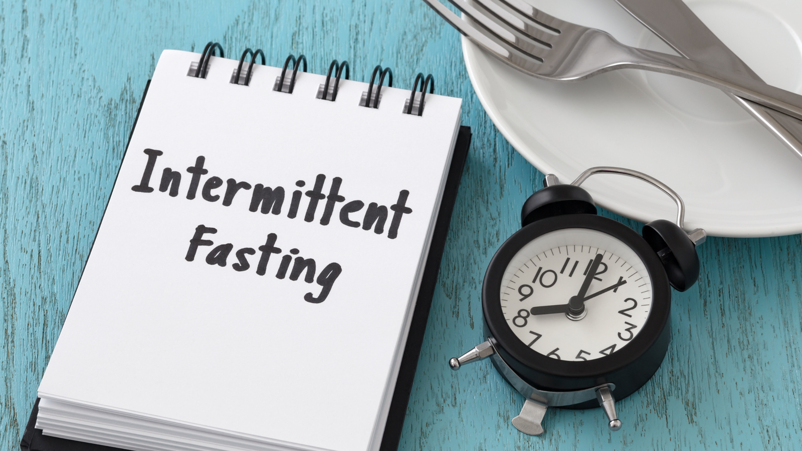 A notepad displaying intermittent fasting knowledge alongside a plate and fork.