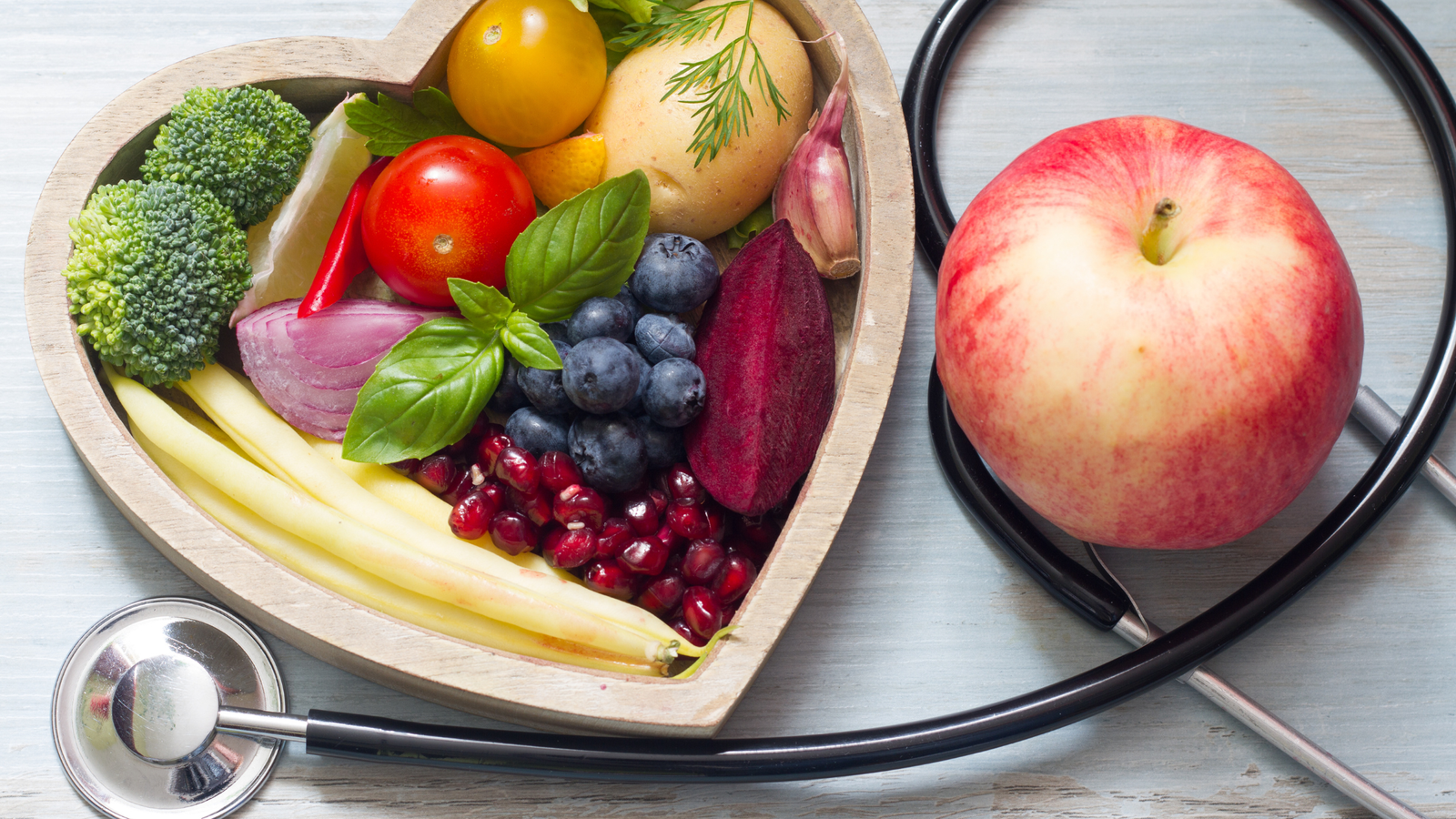 A heart-shaped bowl of fruits and vegetables with a stethoscope, capturing the medical perspective on fasting.